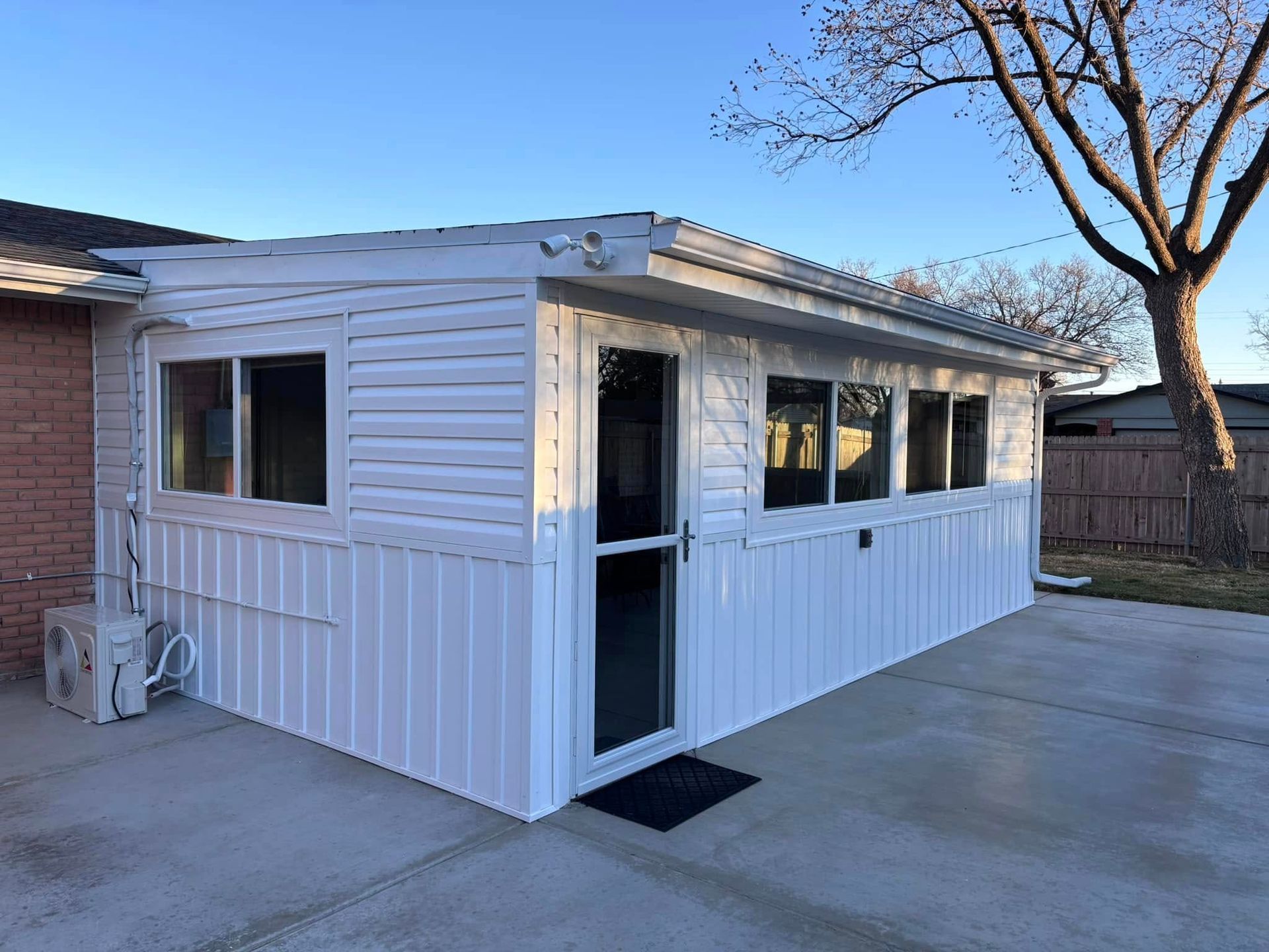 A white shed with a sliding glass door is in the backyard of a house.