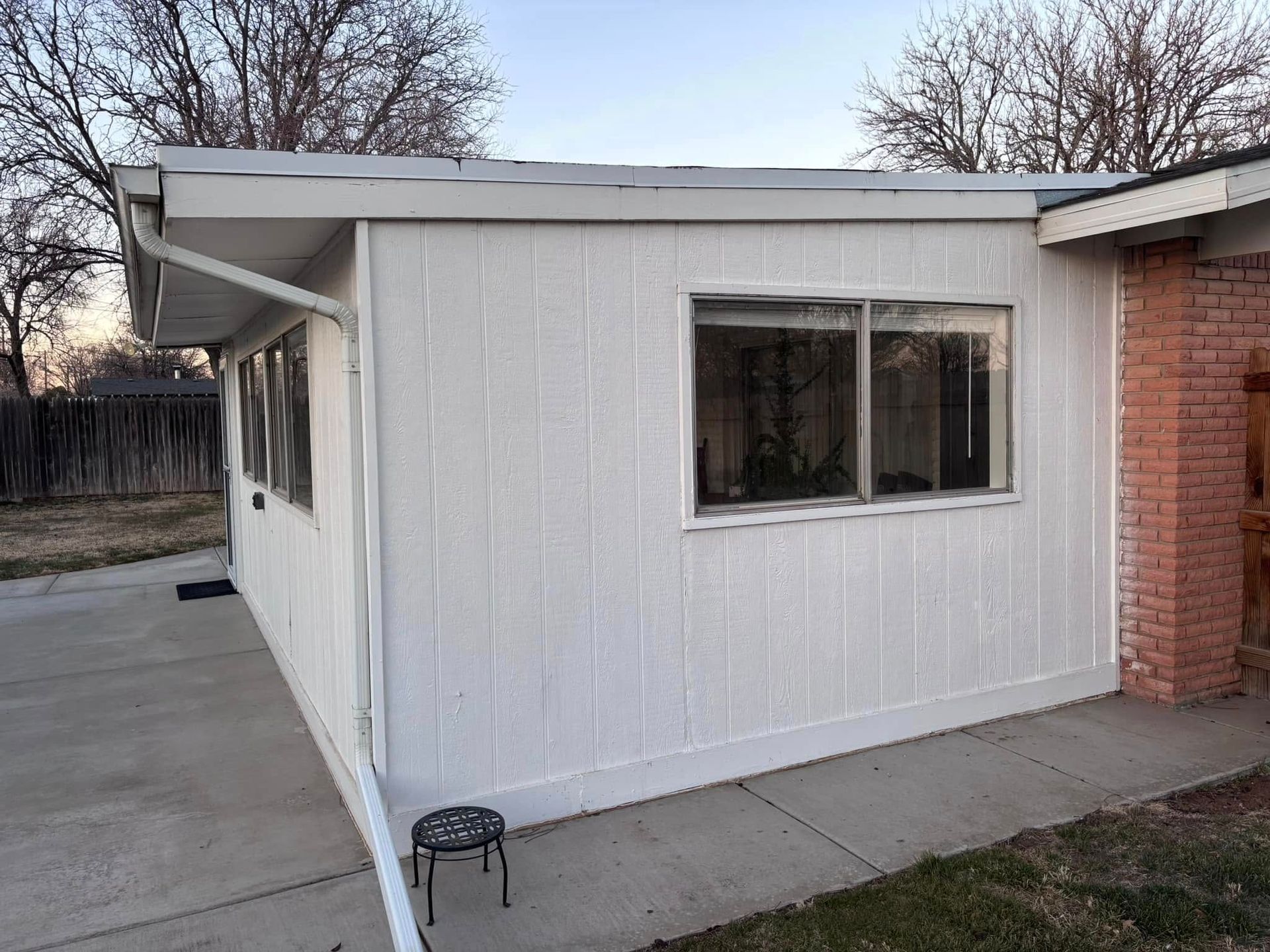 A white house with a brick wall and a stool in front of it.