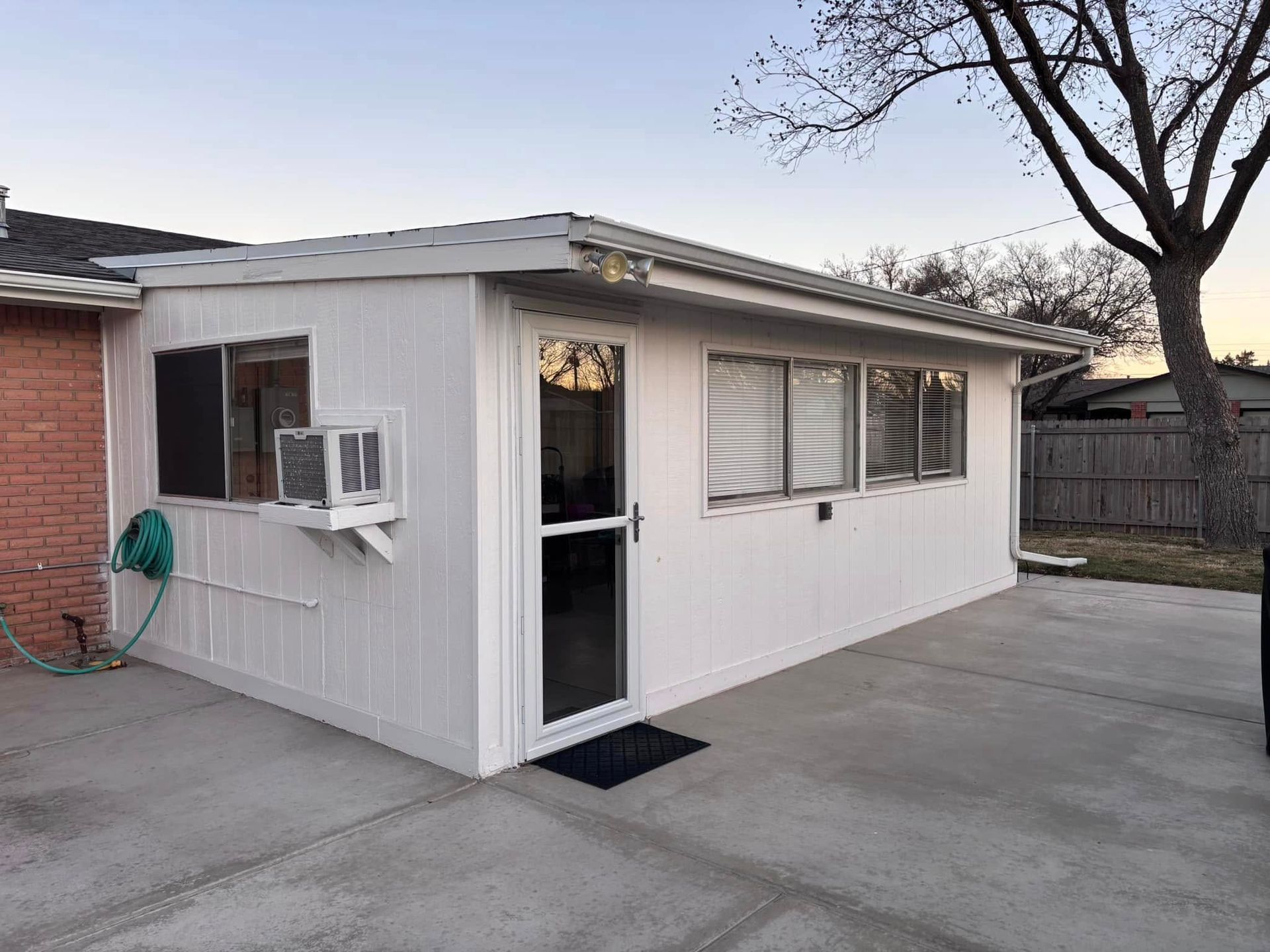A small white house with a window and air conditioner on the side of it.