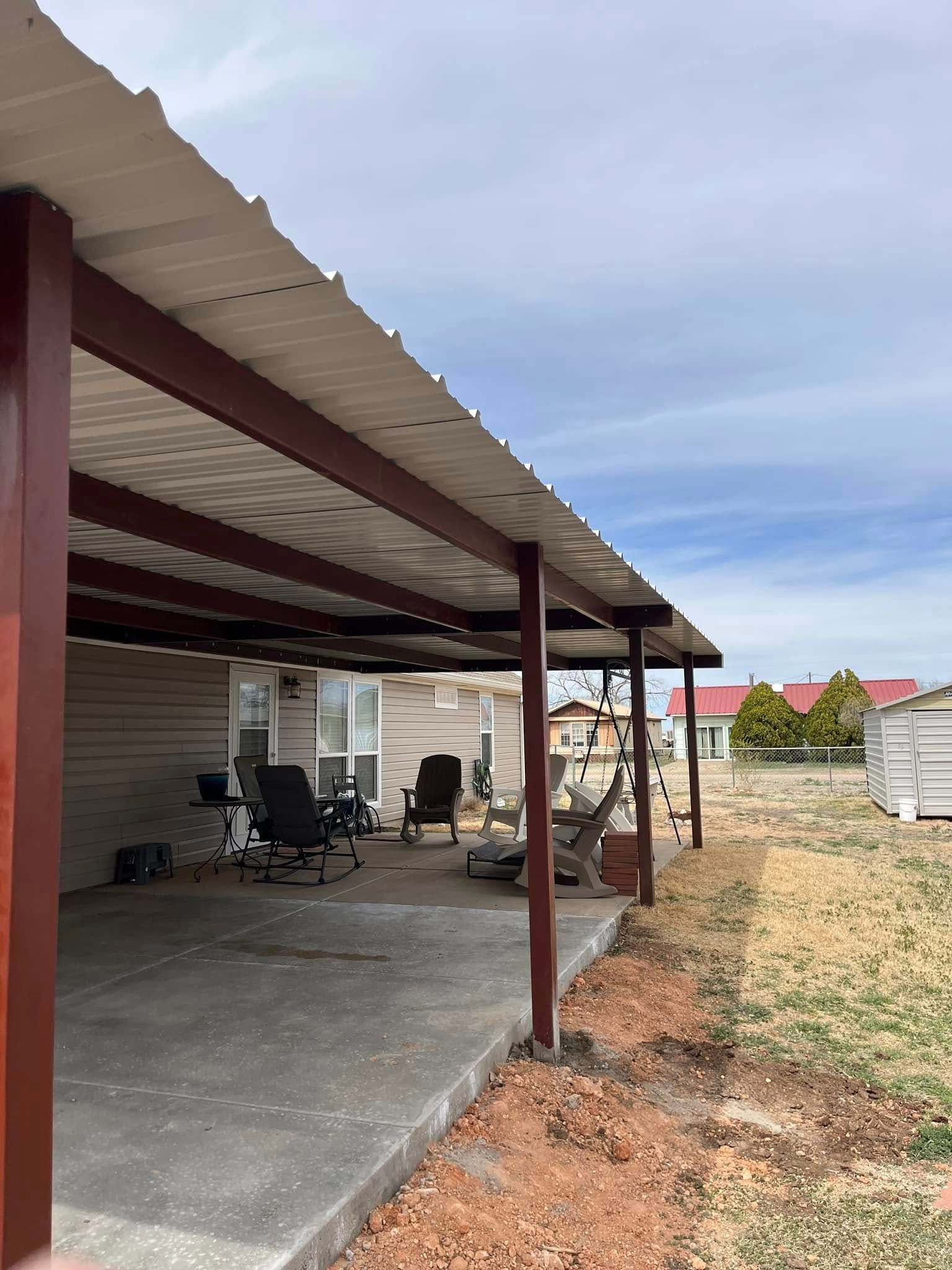 A covered patio with chairs under a metal roof in front of a house.