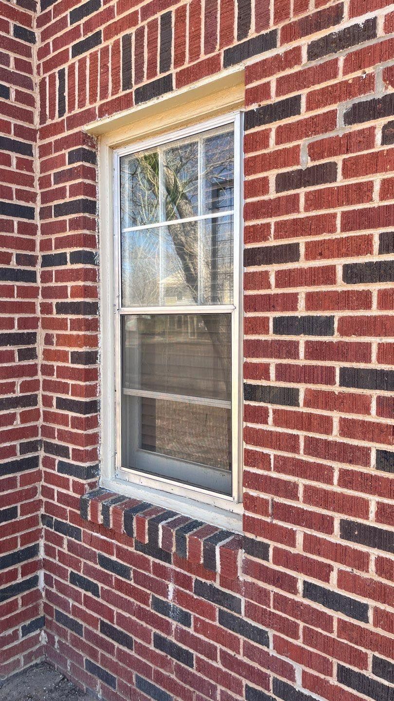 A red and black brick wall with a window in the corner.