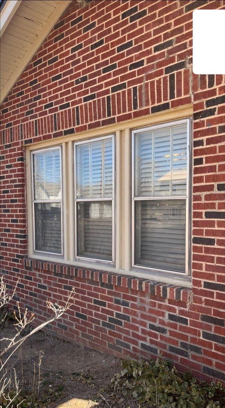 There are three windows on the side of a brick house.