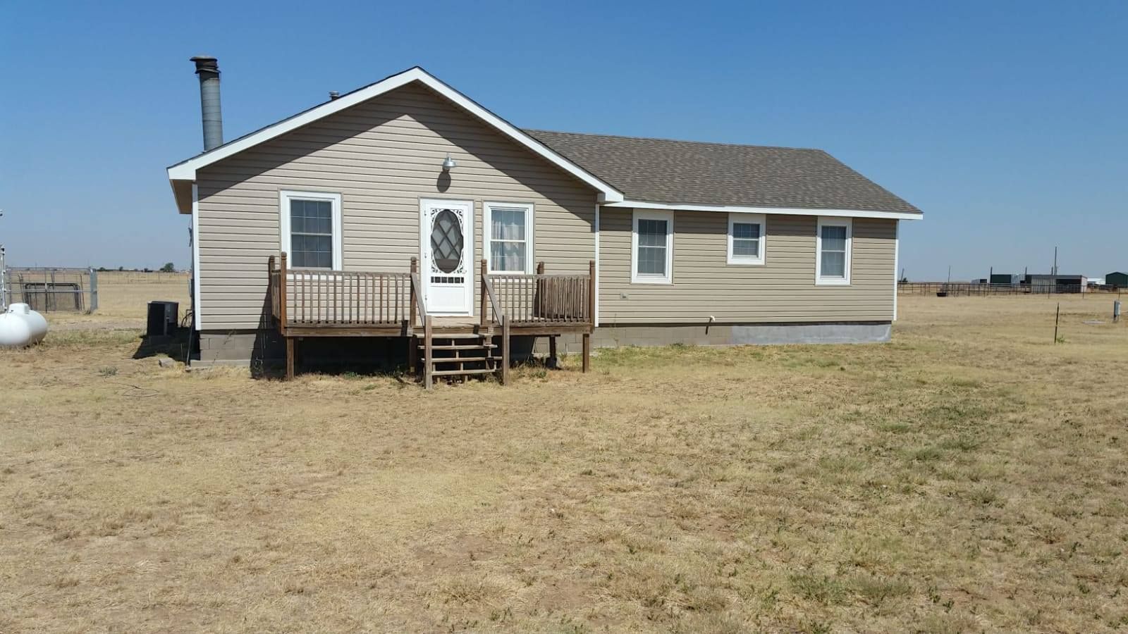 A small house with a deck in the middle of a field.