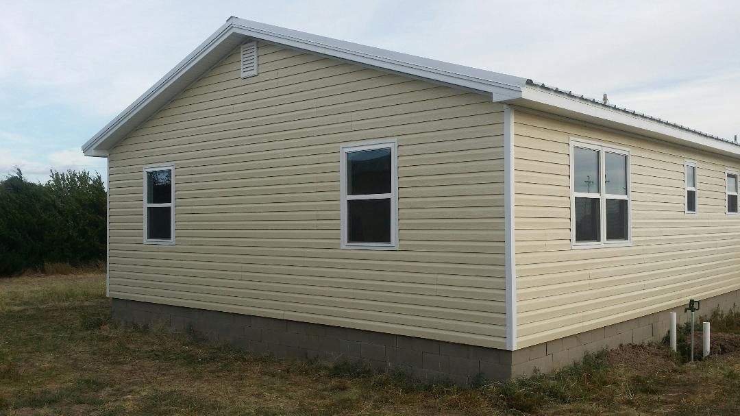 A house with a lot of windows is sitting in the middle of a field.
