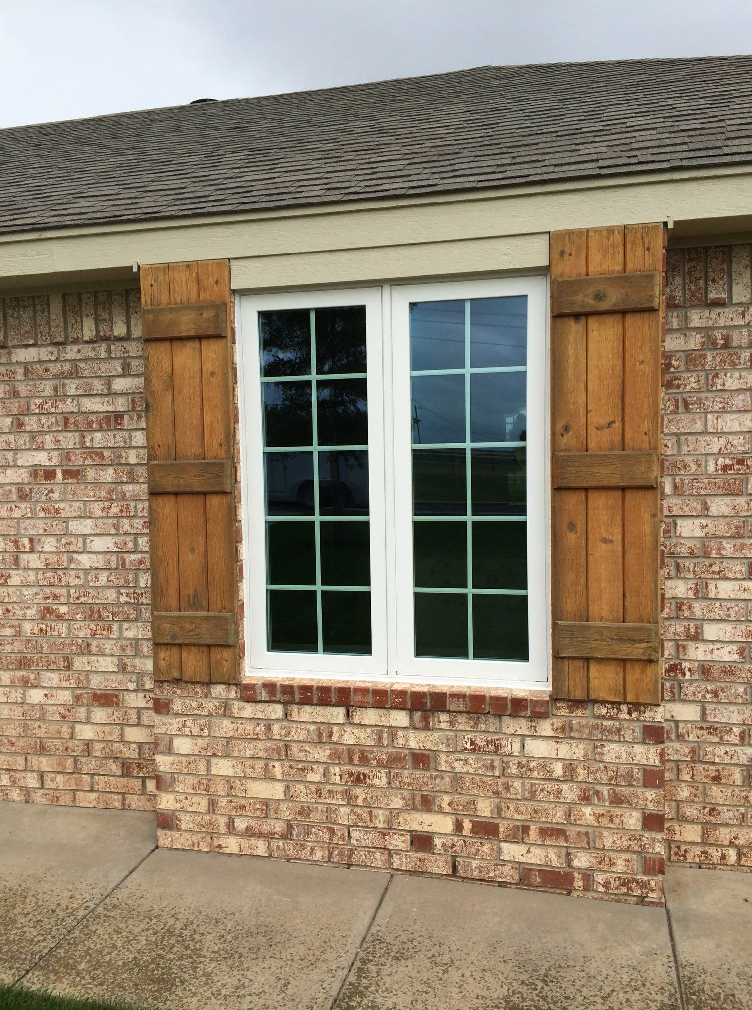 A white window with wooden shutters on a brick house