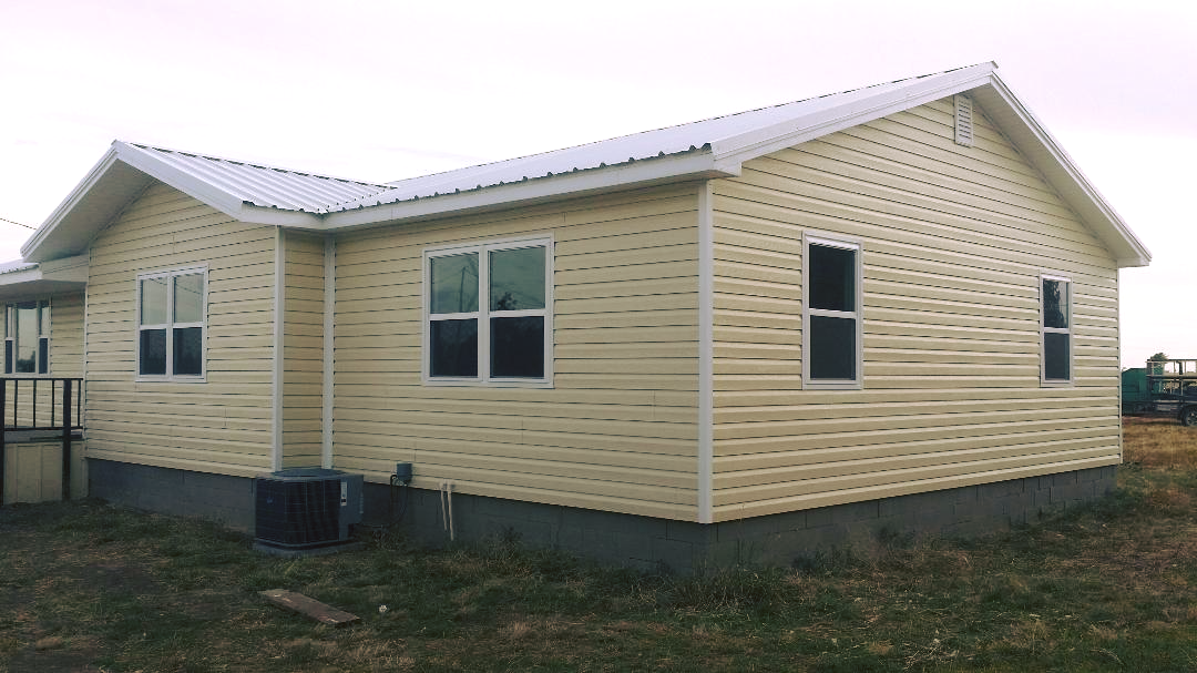 A house with a lot of windows is sitting in the middle of a field.