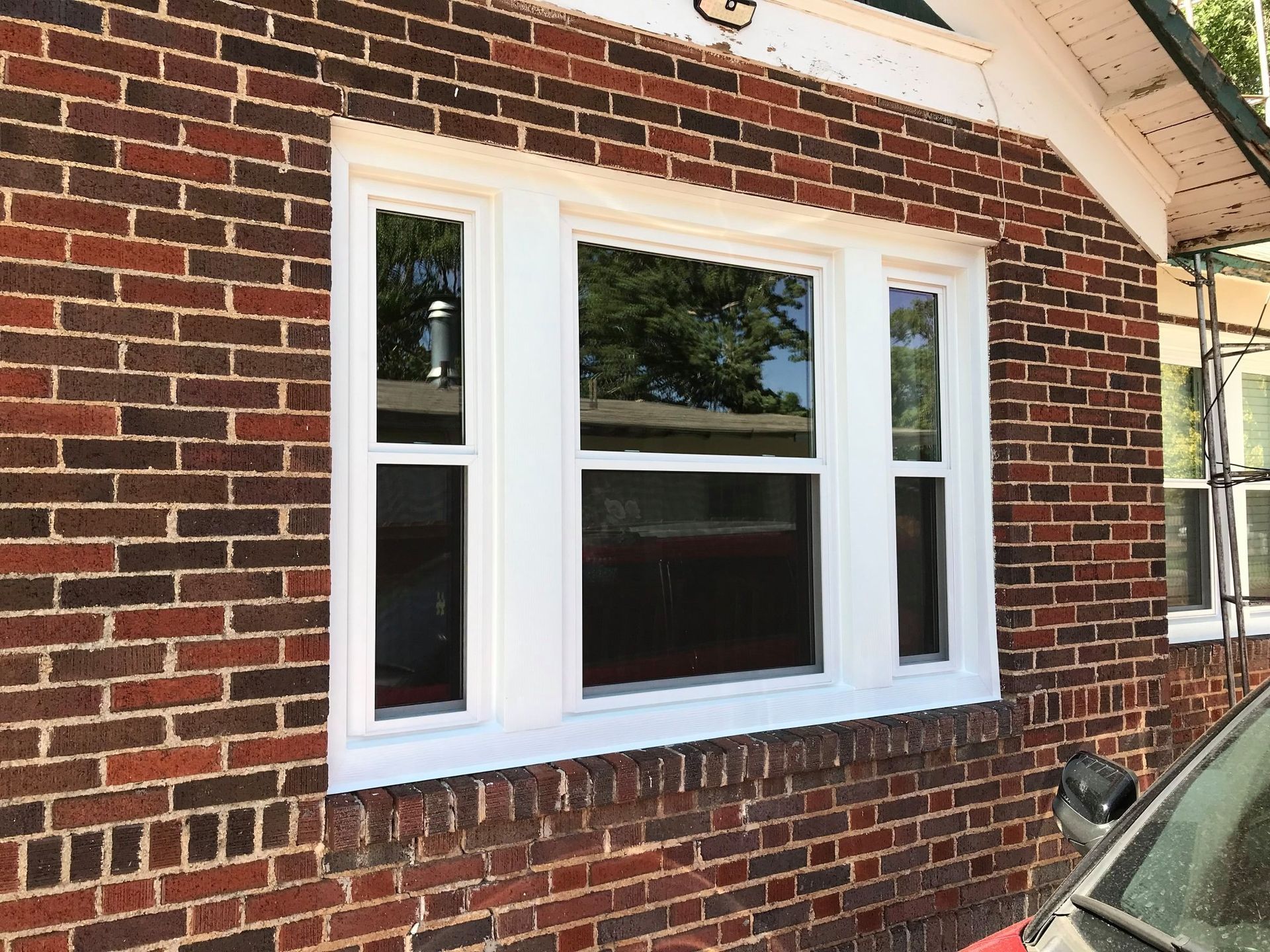 A brick house with a white window and a car parked in front of it.