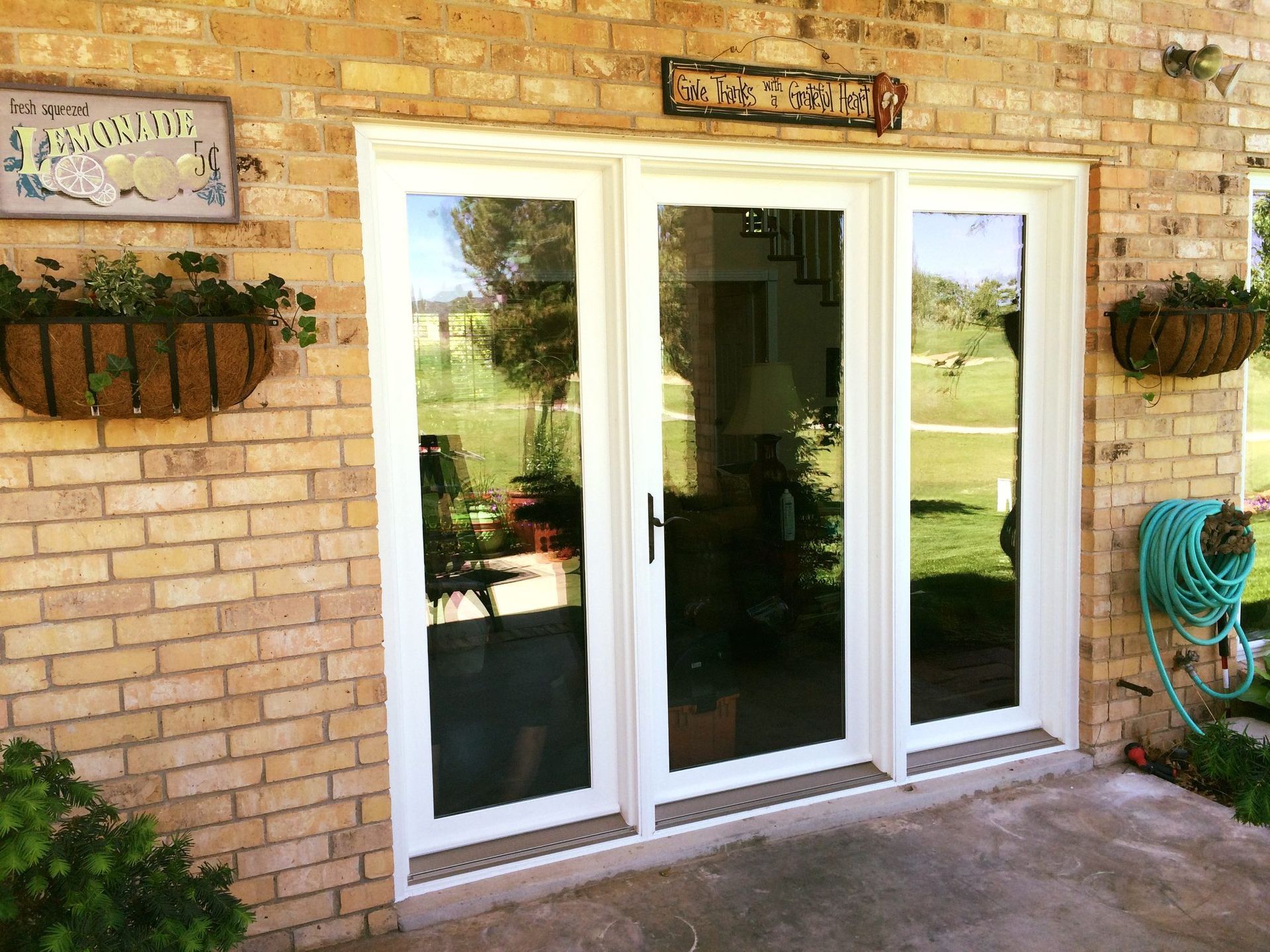 A white sliding glass door is sitting on a brick wall next to a hose.
