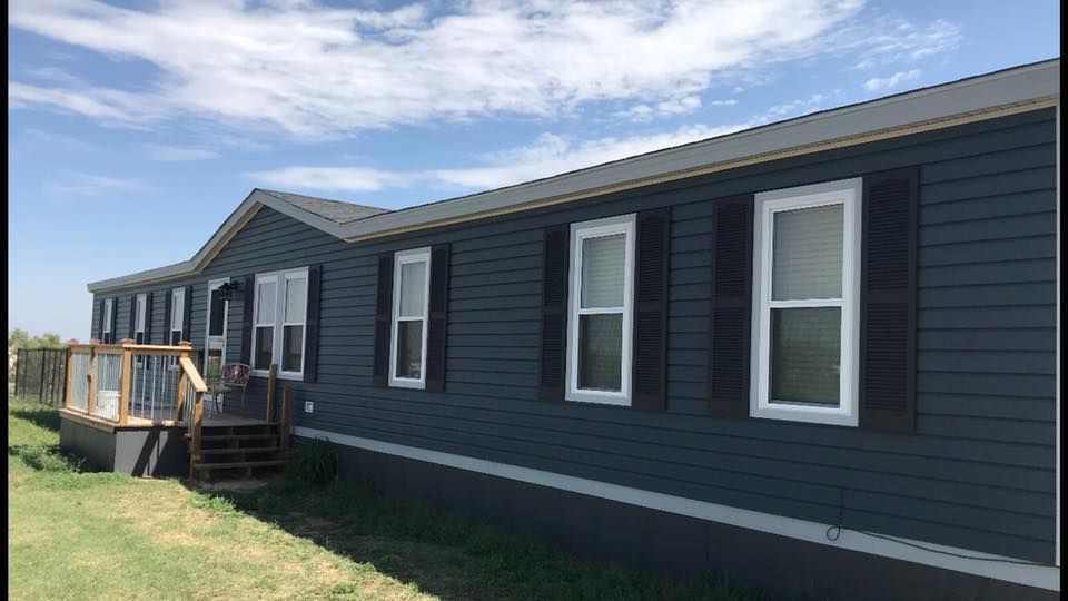 A mobile home with a lot of windows and shutters is sitting on top of a lush green field.