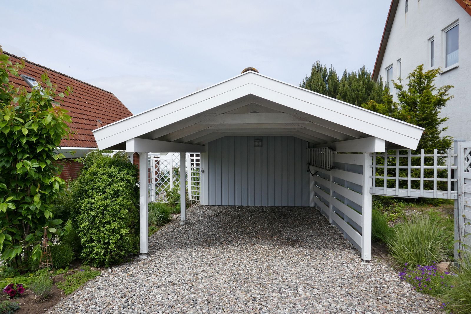 A white carport with a gravel driveway in front of a house.