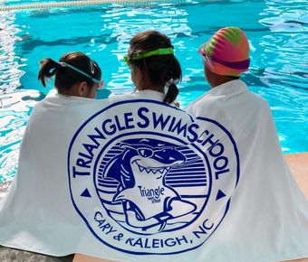 Three children are wrapped in a triangle swim school towel