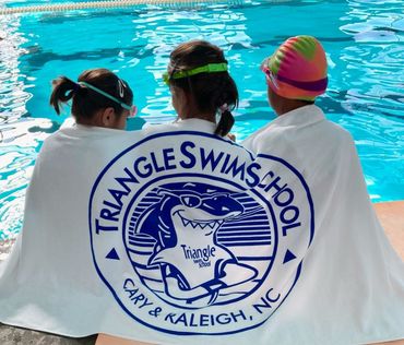 Three children are wrapped in a triangle swim school towel