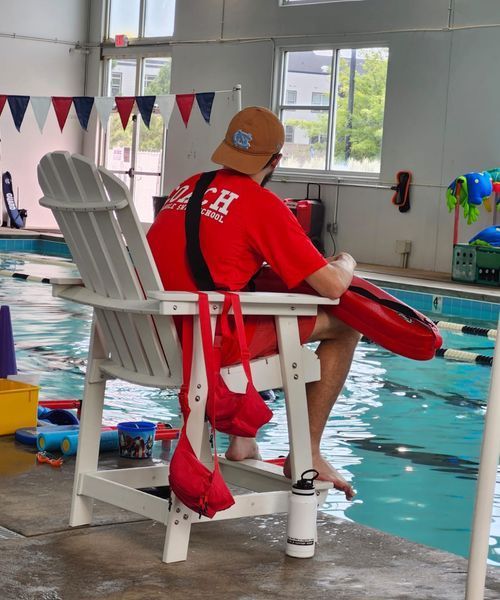 A lifeguard is sitting in a chair near a swimming pool
