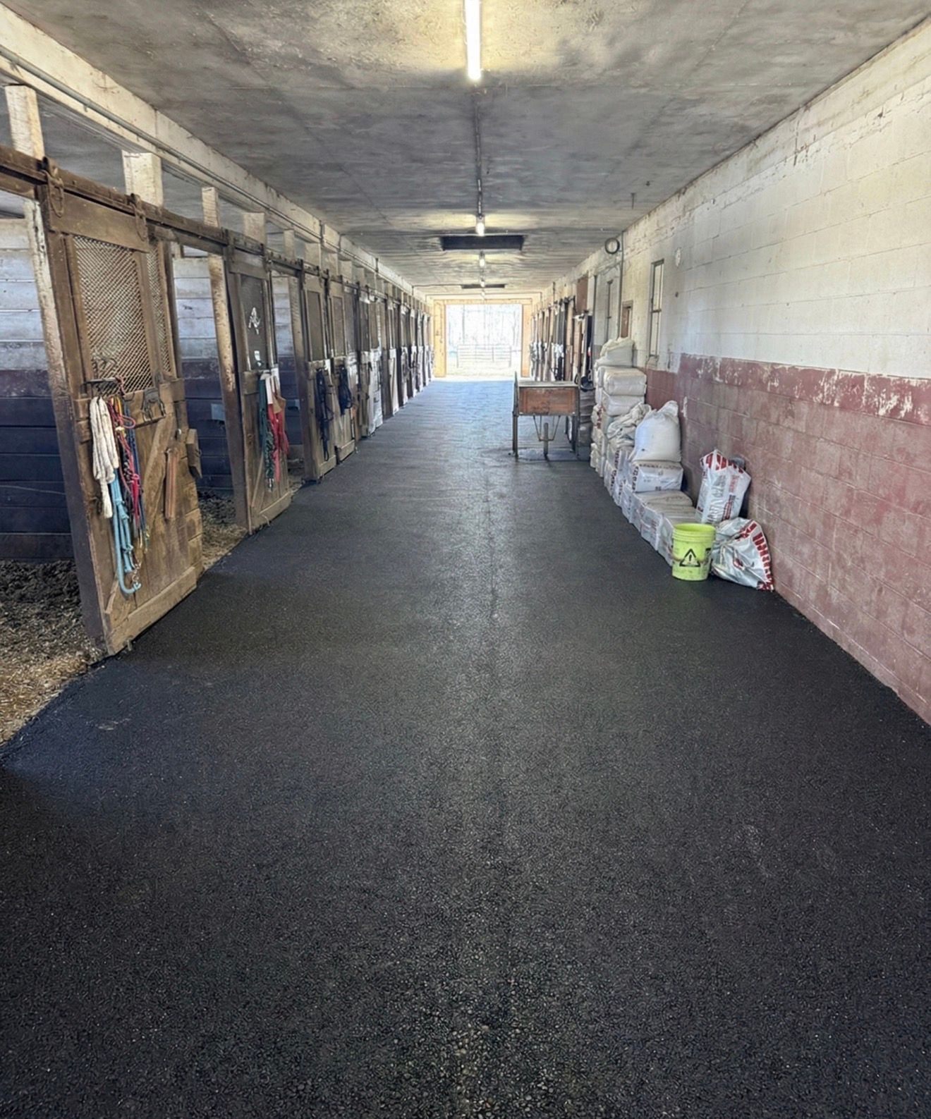 Dim hallway with stalls on the left, white-red walls on the right, and supplies stacked near the end.