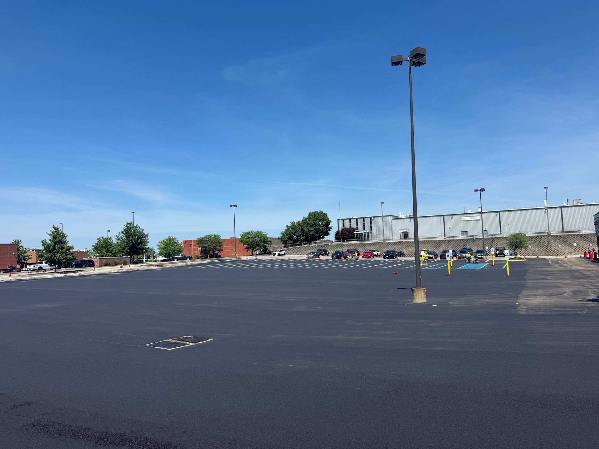 Empty parking lot under a blue sky with a few light poles and distant buildings