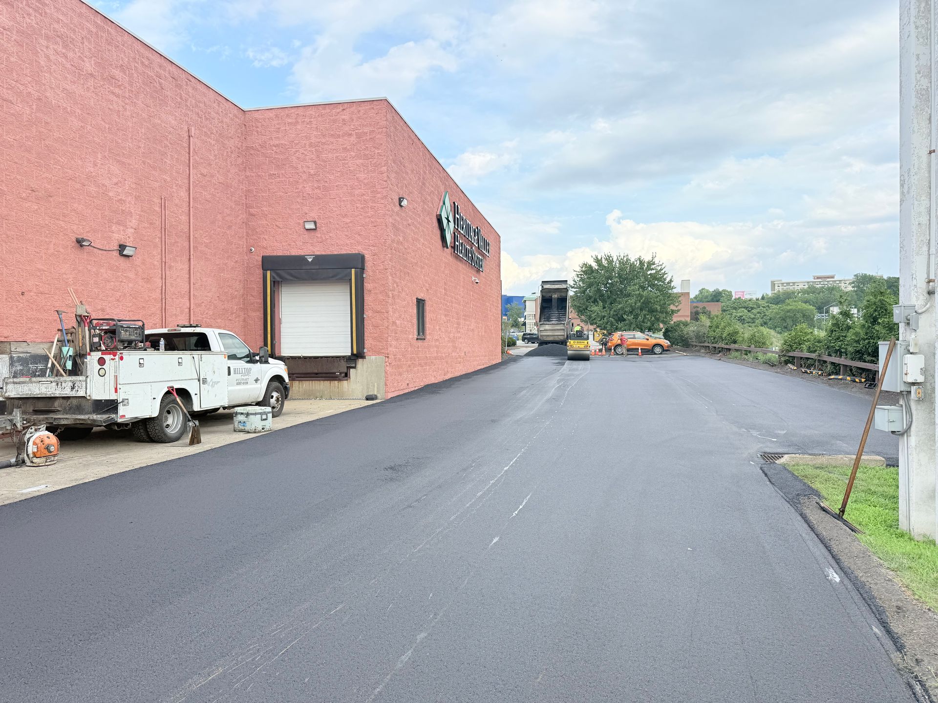 Parking lot beside a pink building, with utility trucks and equipment along an asphalt drive.