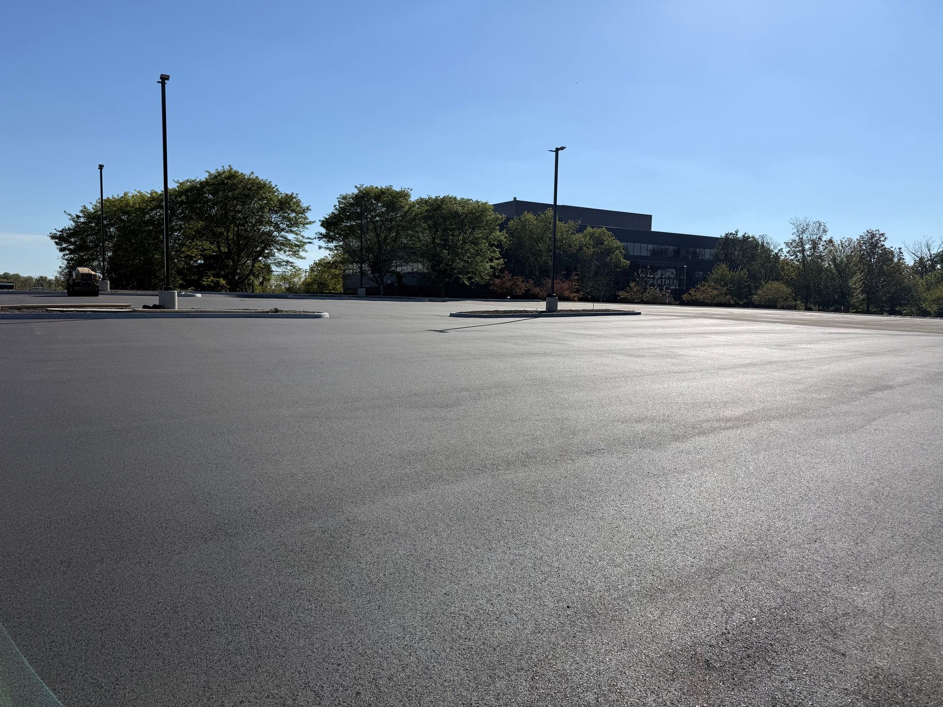 Empty sunlit parking lot with trees and a low building in the distance