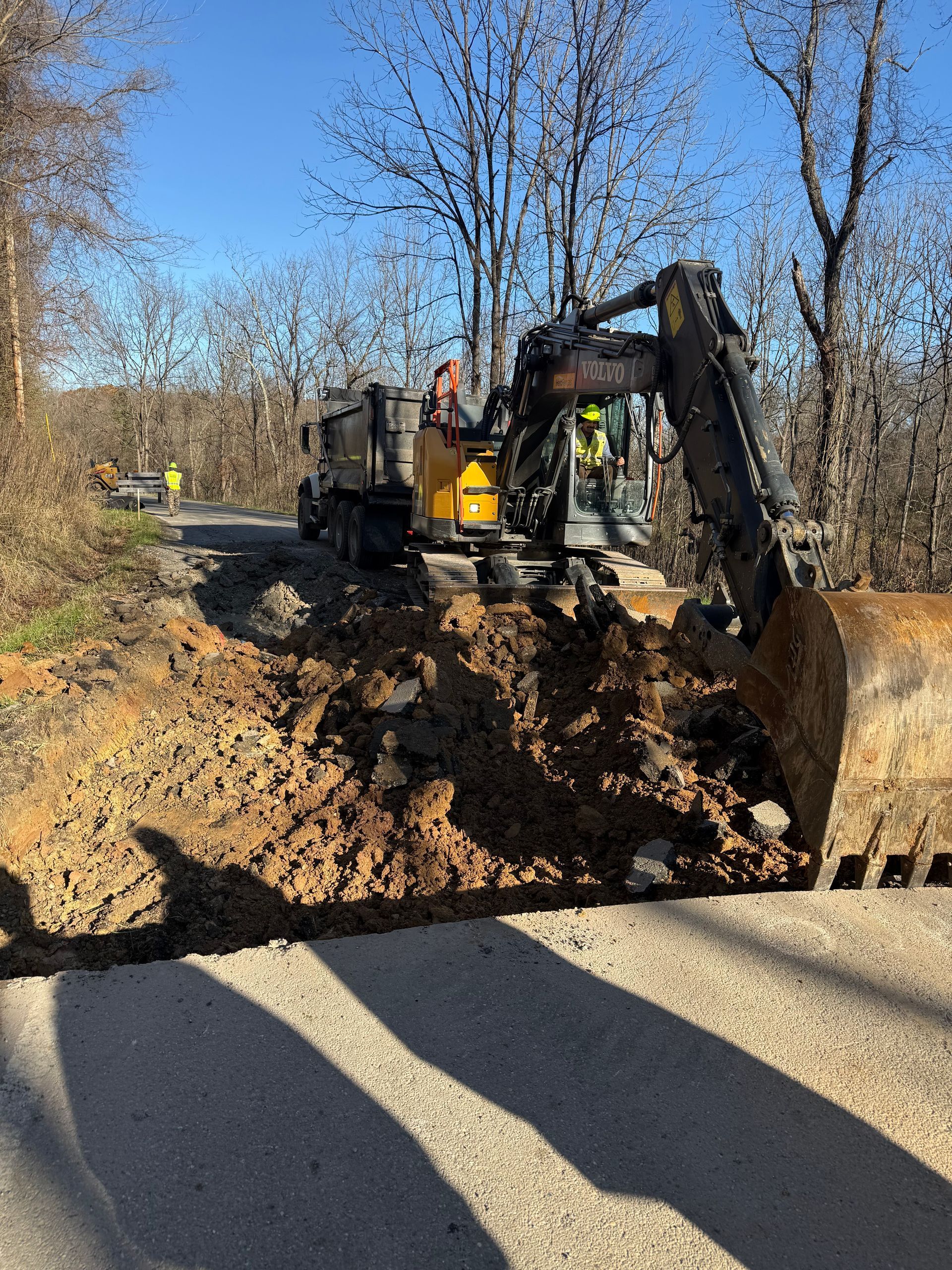 Backhoe excavator digging a trench beside a road on a sunny day