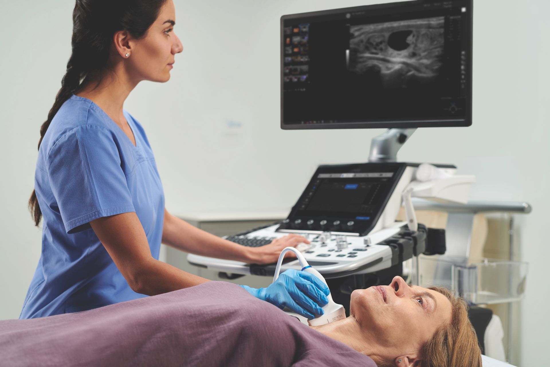 A nurse is examining a patient 's neck with an ultrasound machine.