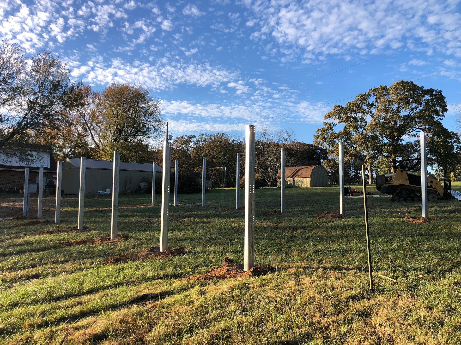 A row of concrete poles in a field with trees in the background.