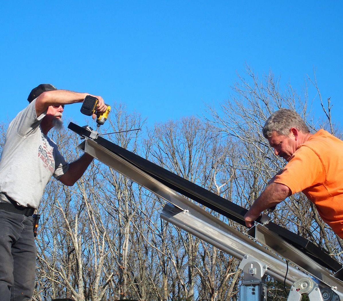 Two men are working on a roof with trees in the background