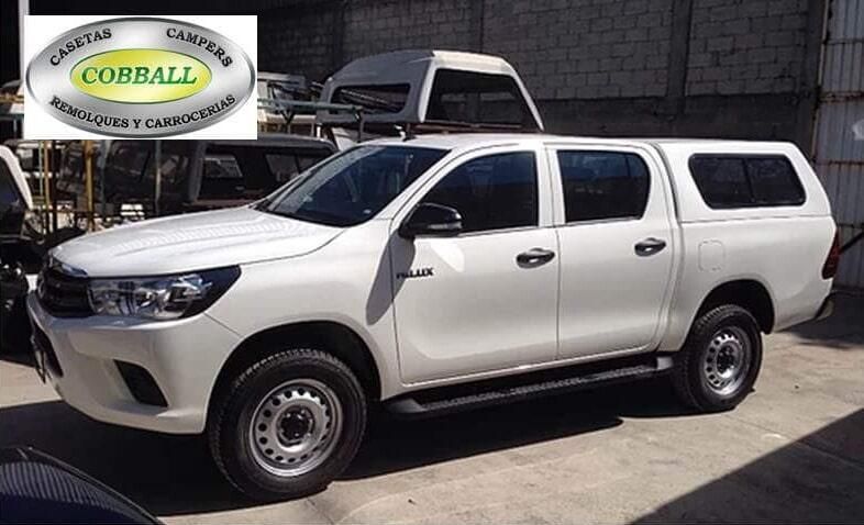 Una camioneta Toyota Hilux blanca con una cubierta para la caja de carga estacionada en un lote, con el logotipo de Cobball visible en una esquina.