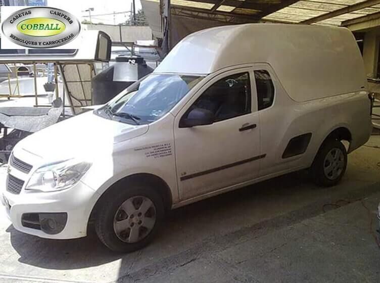 Una camioneta Chevrolet Montana blanca con una gran capota de fibra de vidrio blanca a juego, estacionada en un taller.