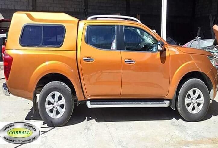 Una camioneta Nissan Navara naranja con una cubierta para la caja de la camioneta estacionada en un garaje cubierto.