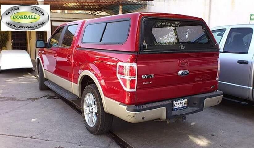 Una camioneta Ford roja con una capota a juego estacionada en un lote de concreto, mostrando su perfil trasero y lateral.