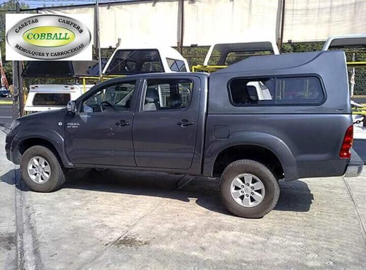Una camioneta Toyota Hilux de doble cabina de color gris oscuro con una capota a juego, estacionada en un aparcamiento al aire libre.