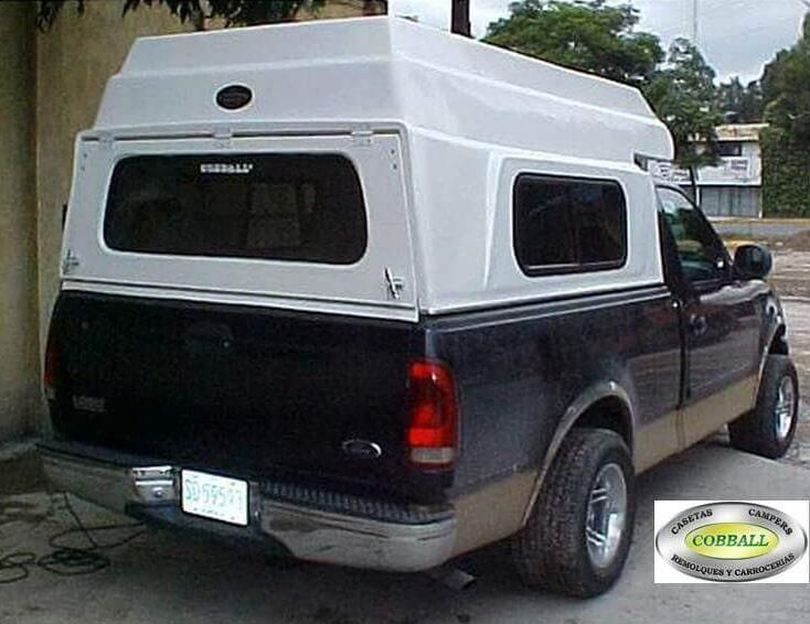Una camioneta Ford de color negro y beige con una capota de fibra de vidrio blanca elevada estaba estacionada afuera.