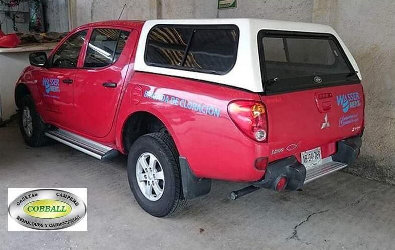 Una camioneta Mitsubishi L200 roja con una capota blanca estacionada en un garaje, junto al logotipo de la empresa de servicios Corball.