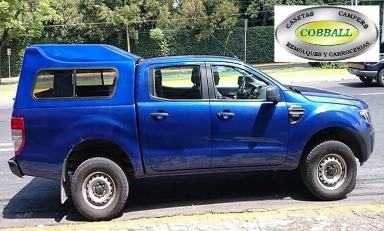 Una camioneta Ford Ranger azul con una capota a juego, estacionada en una calle con el logotipo de Cobball en una esquina.