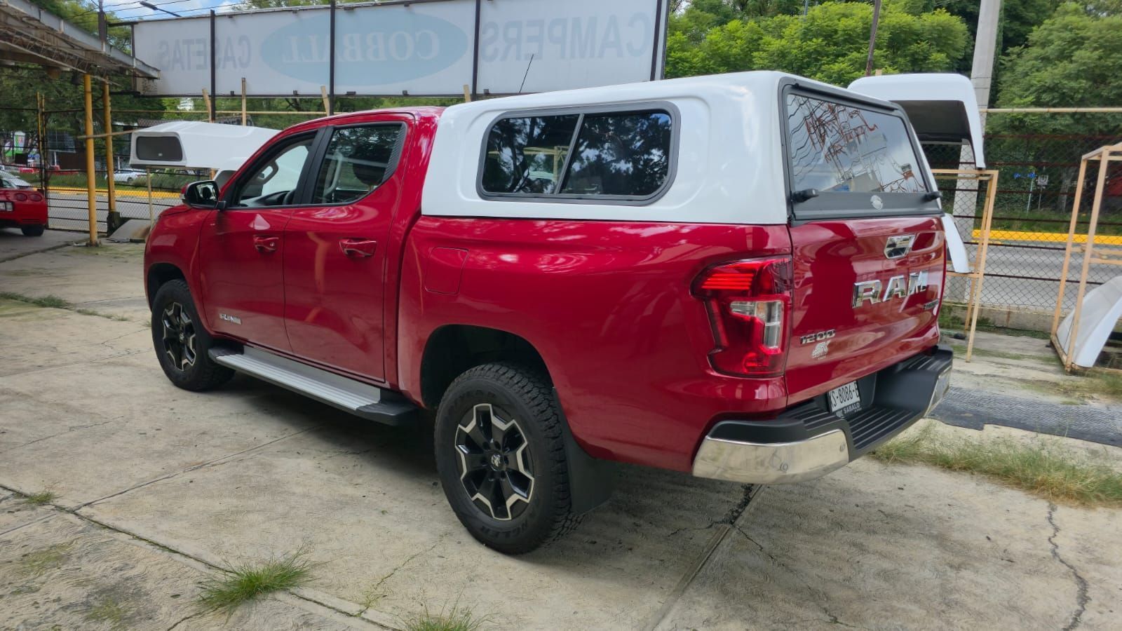 Una camioneta roja con una caja de carga blanca estacionada en un terreno pavimentado.