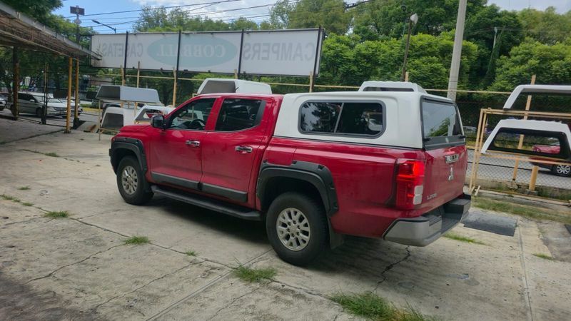 Una camioneta roja con una caja de carga blanca estacionada en un terreno pavimentado.