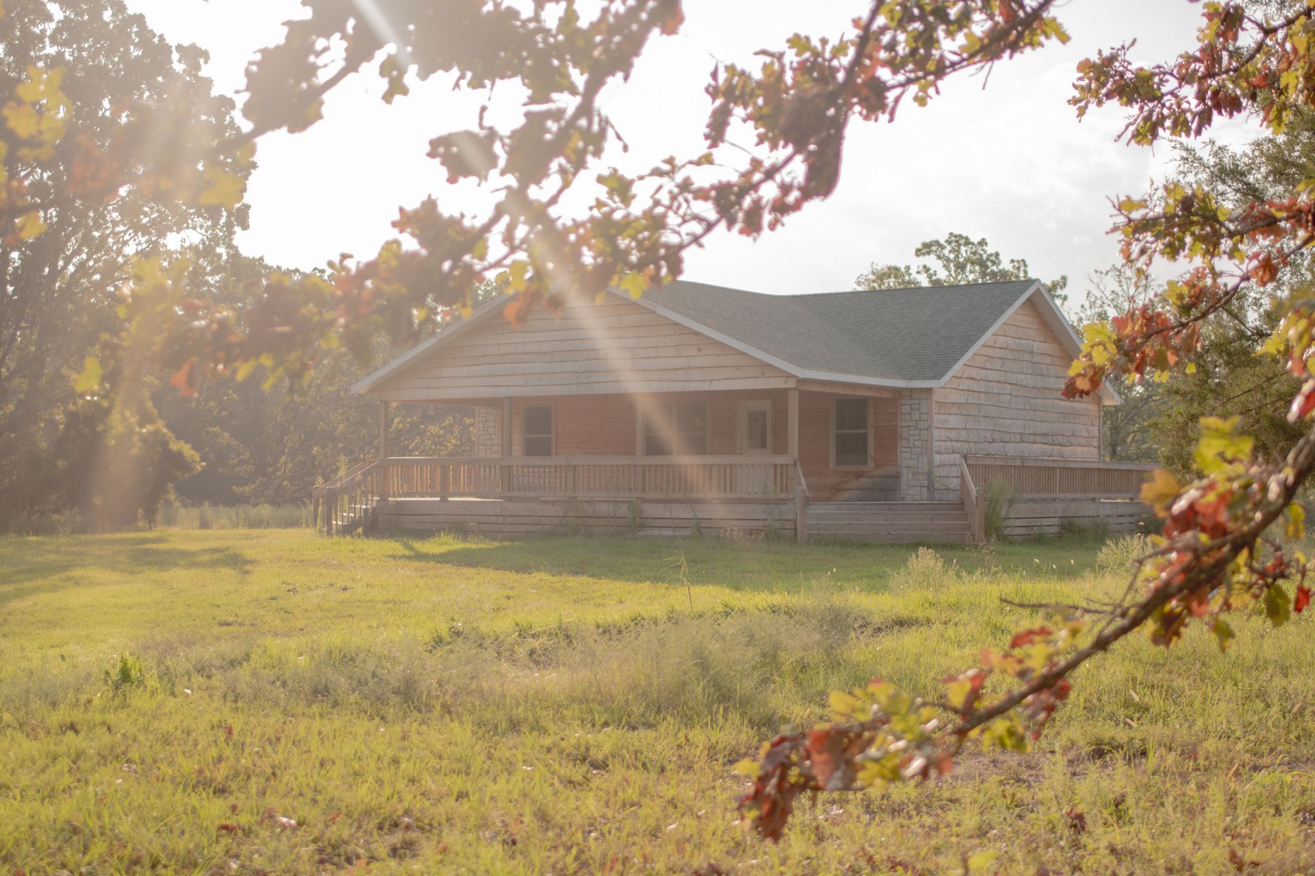 A house in the middle of a field with the sun shining through the trees