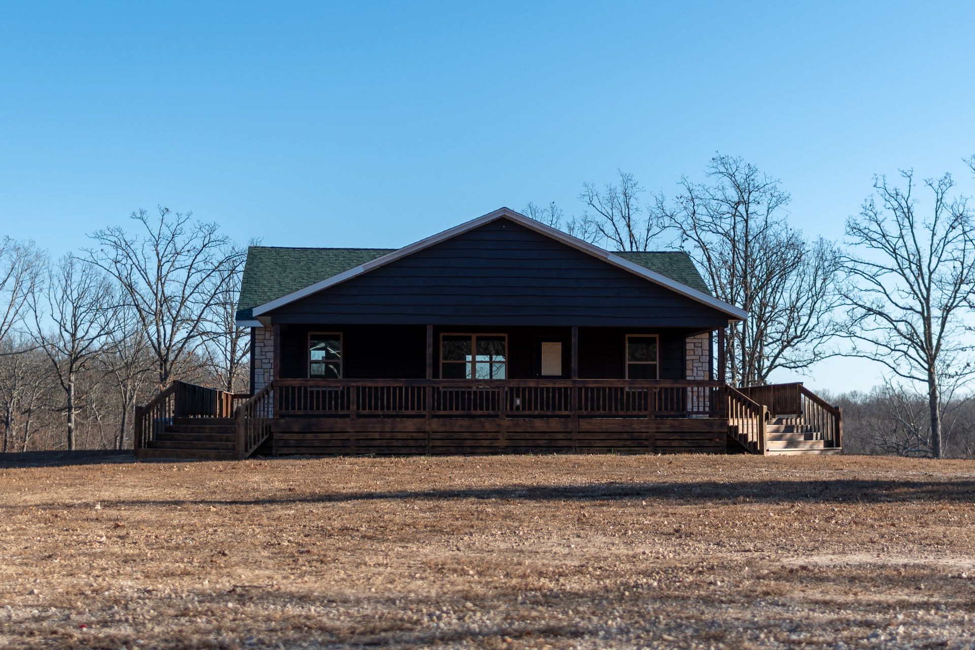 A large house with a large porch is sitting on top of a dry grass field.