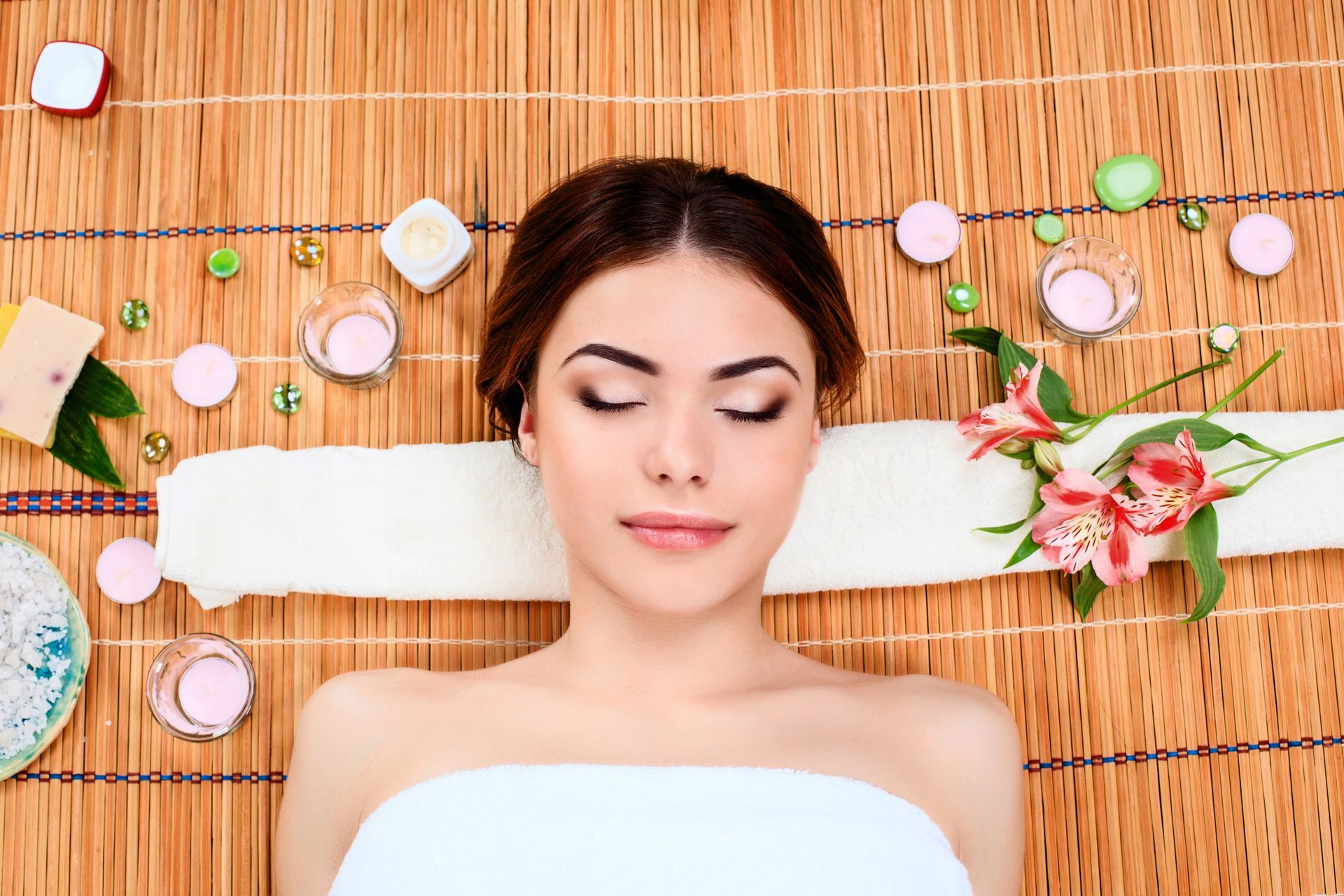 A woman is laying on a bamboo mat in a spa with her eyes closed.