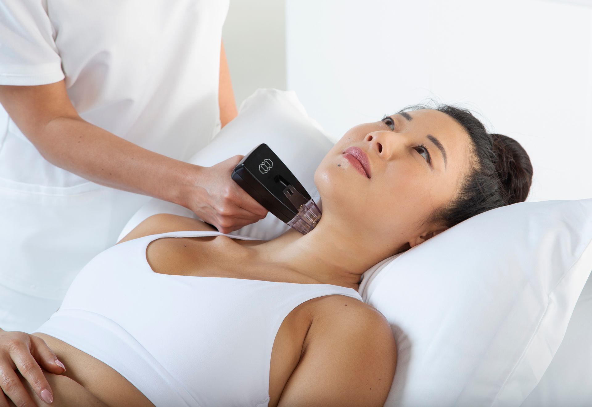 A woman is laying in a bed getting a treatment on her neck.