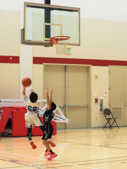 Basketball player in white jersey driving to the hoop as a defender contests in a gym