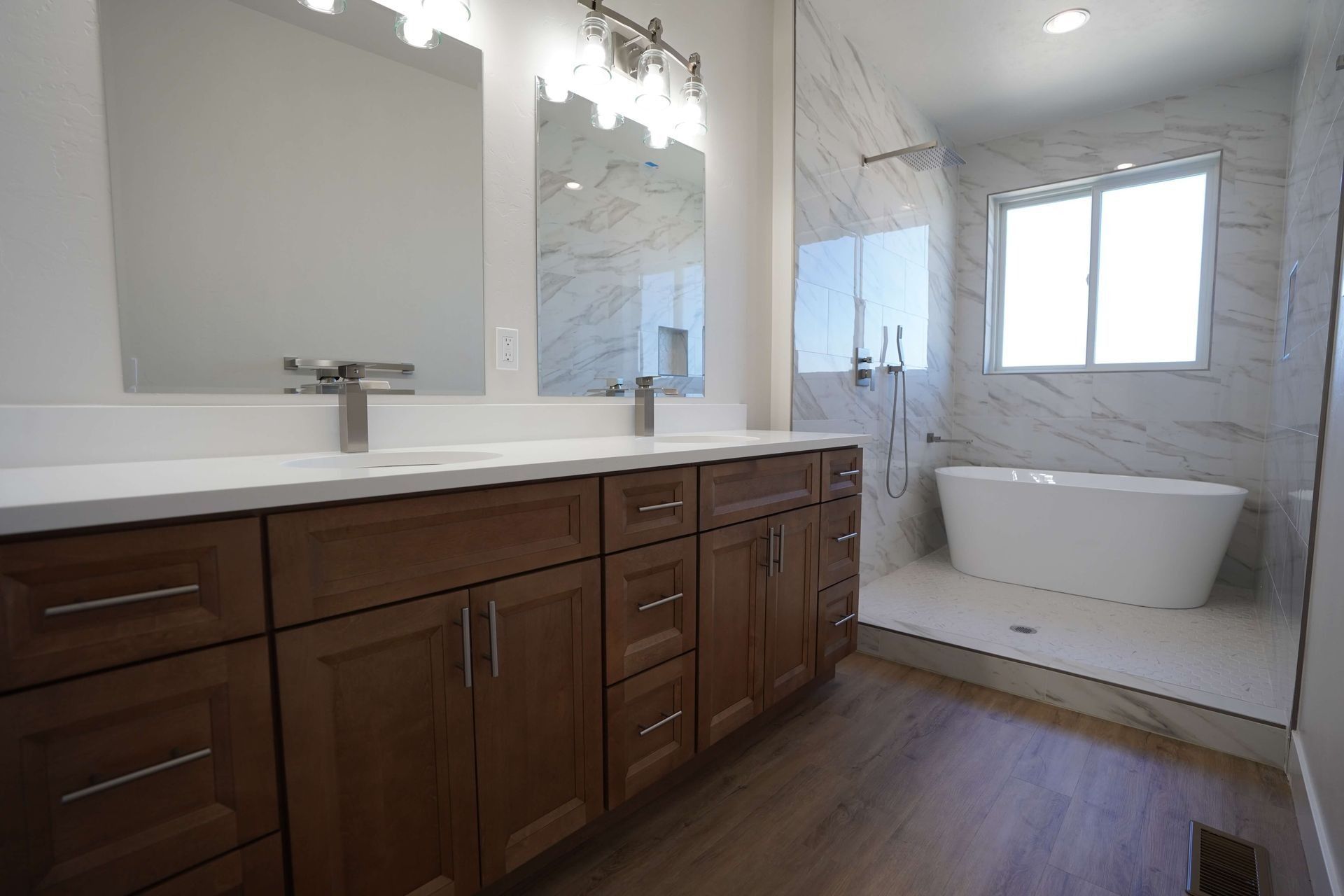 A modern bathroom with wood cabinets, double vanity mirrors, and a white freestanding tub in a marble walk-in shower.