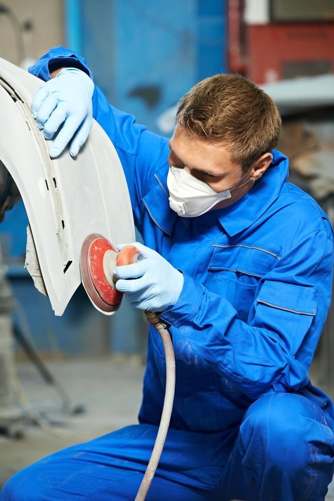 A Man Wearing A Mask And Gloves Is Sanding A Car Fender — Taminda Smash Repairs In Walcha, NSW
