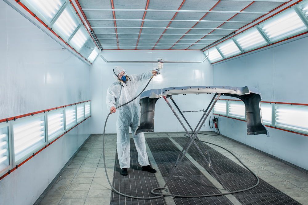 A Man Is Painting A Car In A Paint Booth — Taminda Smash Repairs In Taminda, NSW