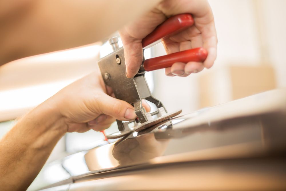 A Person Is Using A Pair Of Pliers To Fix A Car Door — Taminda Smash Repairs In Gunnedah, NSW