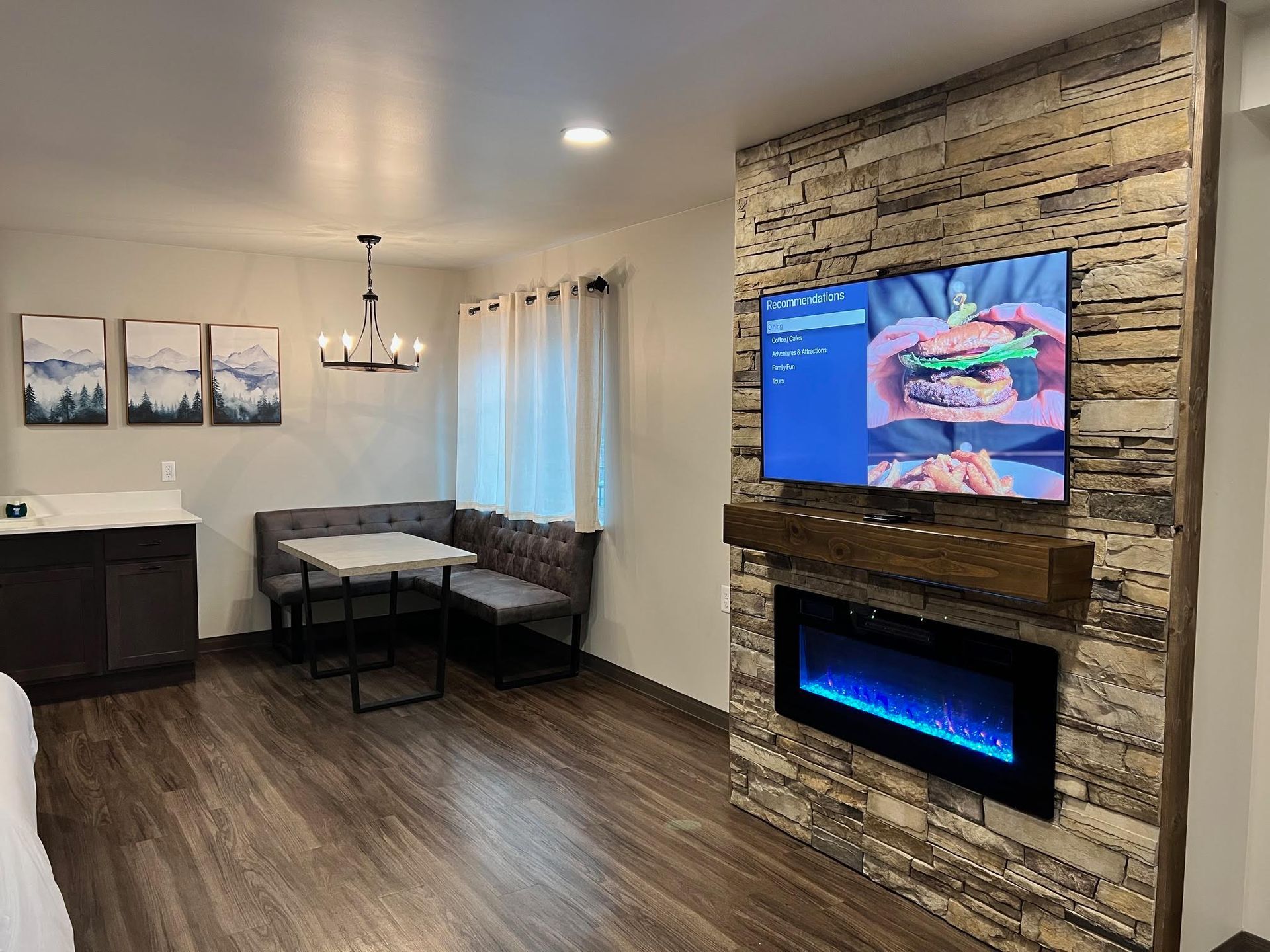 Living room with TV, fireplace, dining area, and artwork on a stone accent wall.