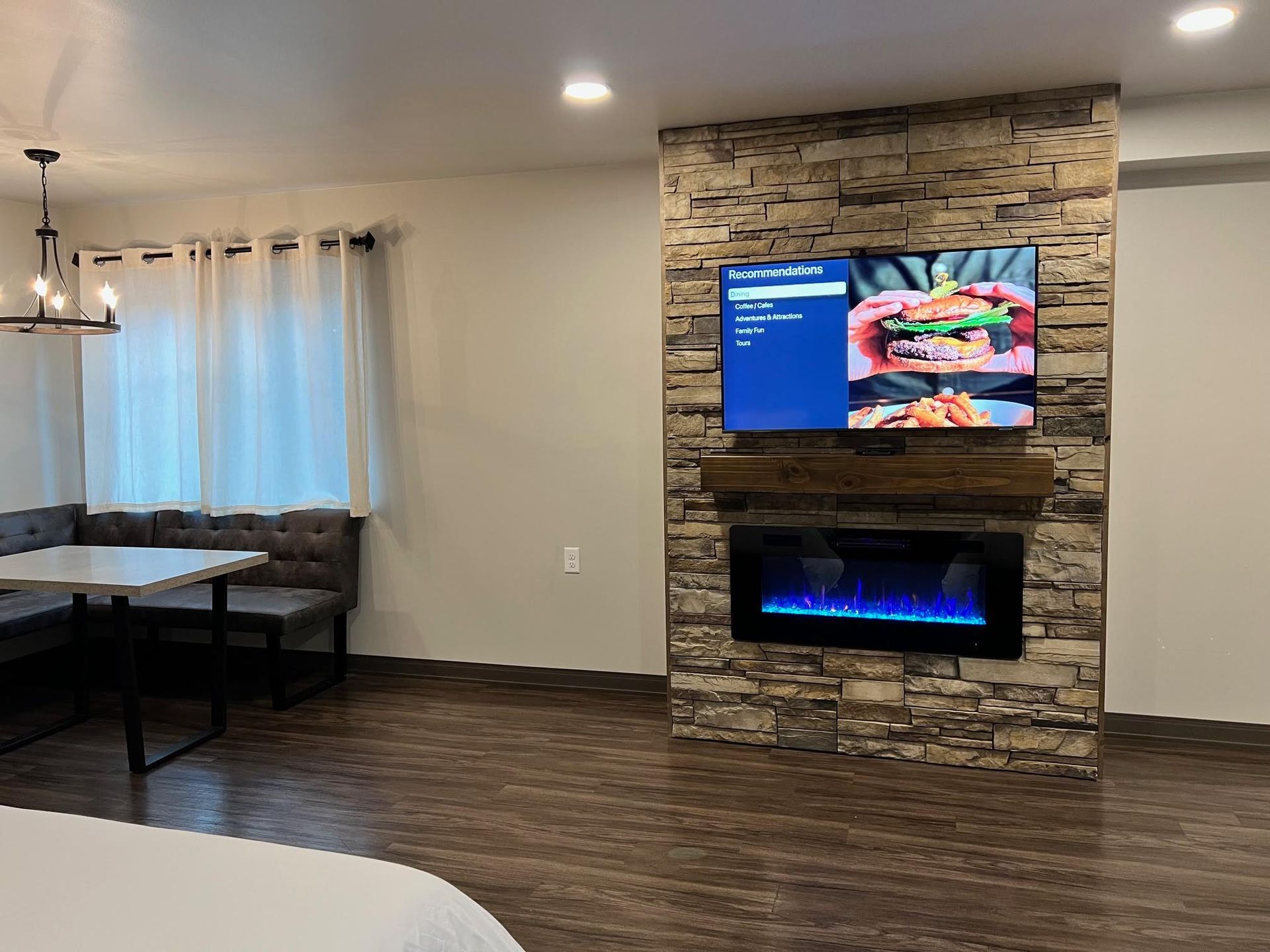 Living area with a mounted TV above an electric fireplace, stone wall, and dining nook.