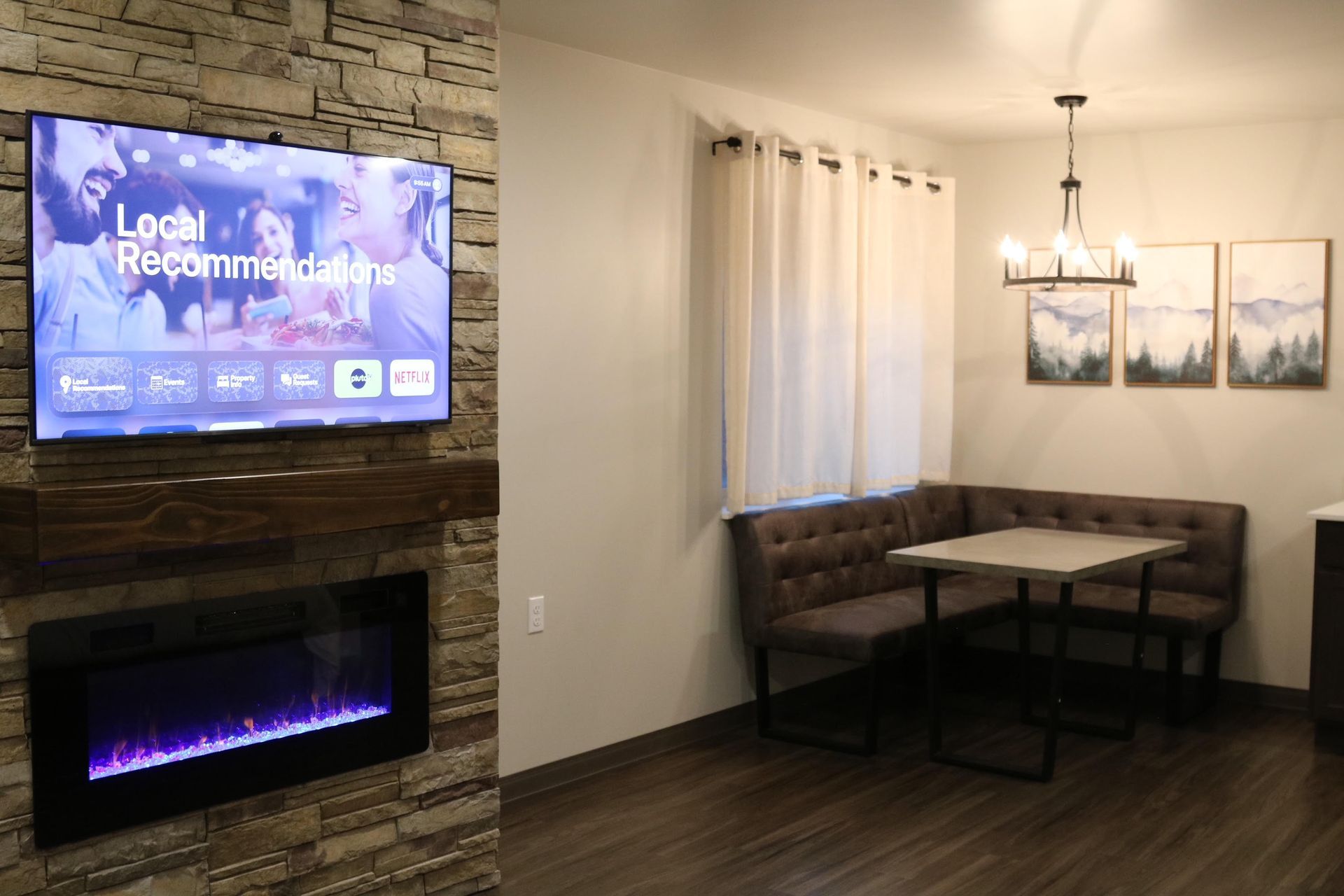 Living room with fireplace, TV, corner booth seating, dining table, and artwork.