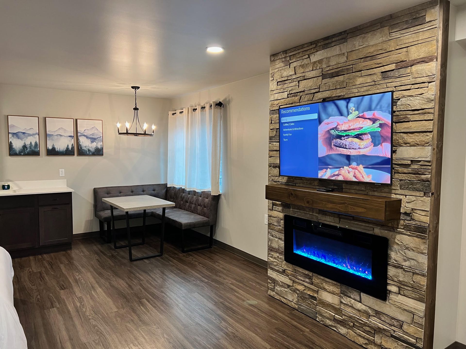 Living space with TV on a stone wall above a fireplace, table, and seating.