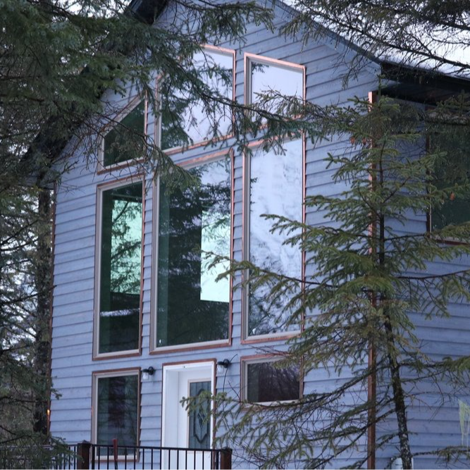 Blue house with large, multi-pane windows and a white door, set amongst trees.