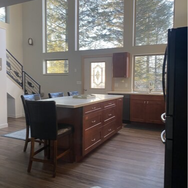 Modern kitchen with island, cabinets, tall windows, and a dark refrigerator.